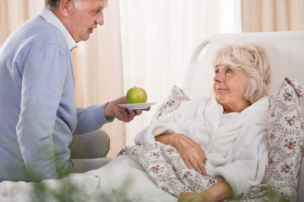 Senior reicht bettlägerigen Seniorin (Verhinderungspflege) einen Apfel