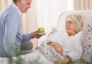 Senior reicht bettlägerigen Seniorin (Verhinderungspflege) einen Apfel