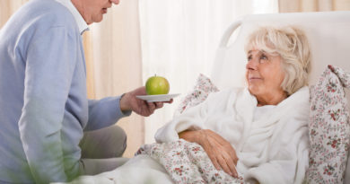 Senior reicht bettlägerigen Seniorin (Verhinderungspflege) einen Apfel