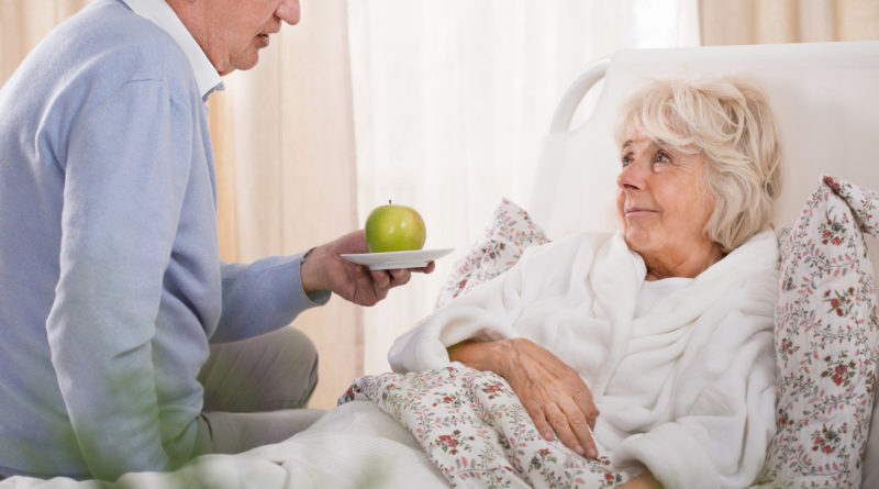 Senior reicht bettlägerigen Seniorin (Verhinderungspflege) einen Apfel